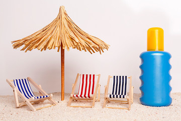 Toy chaise longue and sun umbrella on sandy beach at the white background. Relaxation concept.
