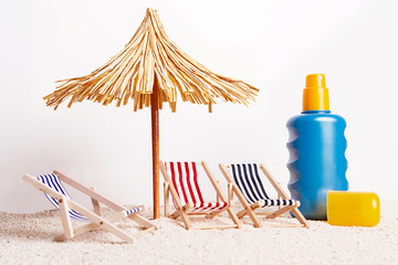 Toy chaise longue and sun umbrella on sandy beach at the white background. Relaxation concept.