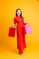 Fototapeta na wymiar Vietnamese woman wearing traditional ao dai clothes and holding shopping bags in Tet festival on white background