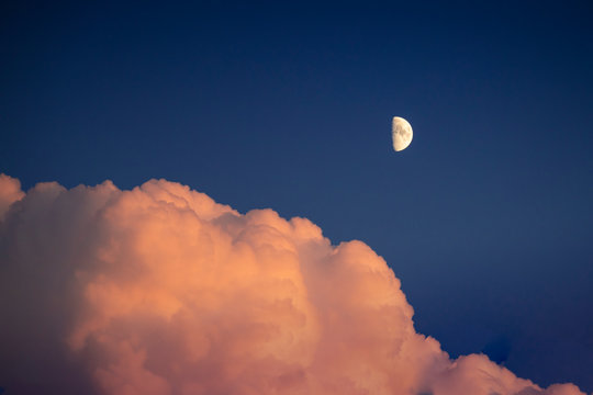 Pastel tones sky at blue hour, with pink fluffy clouds and half moon.