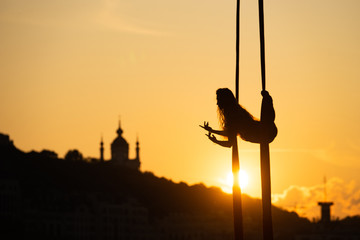 Silhouette of a flexible woman acrobat on aerial silk during a sunset on Kiev city background. concept of freedom and peace