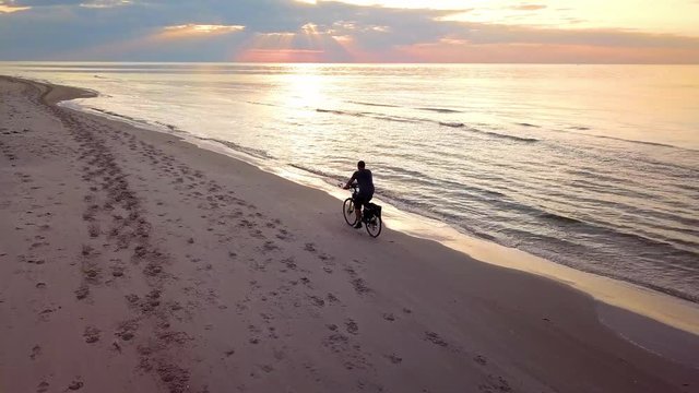 Aerial Slowmotion Shot of a Young Man Riding Bicykle on Beach at Sunset. Beach Bicykle Ride.