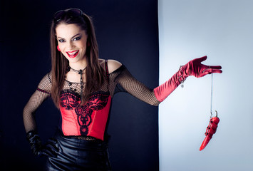 the girl in the red corset laughs and keeps on the chain of red pepper. Conceptually. Erotic game.