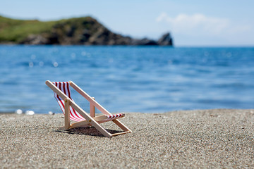 Fototapeta na wymiar Toy chaise longue on sandy beach on sunny day at the blue sea background. Relaxation concept.