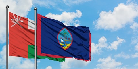 Oman and Guam flag waving in the wind against white cloudy blue sky together. Diplomacy concept, international relations.