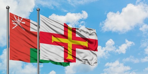 Oman and Guernsey flag waving in the wind against white cloudy blue sky together. Diplomacy concept, international relations.