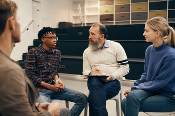 Young people sitting and telling their stories to the senior man while he making notes in document