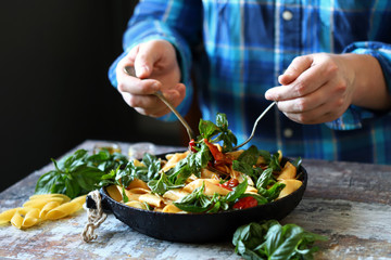 Hands of the chef mix the pasta in a pan. One pan pasta. Vegan pasta with basil. Selective focus. Macro.