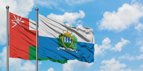 Oman and San Marino flag waving in the wind against white cloudy blue sky together. Diplomacy...