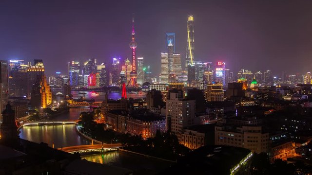Timelapse illuminated Shanghai buildings and skyscrapers behind Waibaidu Bridge over Wusong river with sailing motorboats in China at night