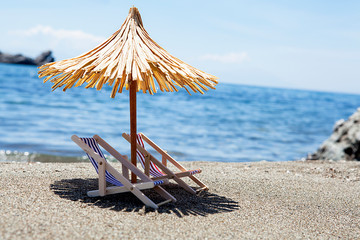 Toy chaise longue and sun umbrella on sandy beach on sunny day at the blue sea background....