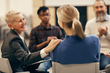 Smiling mature woman with short hair talking to the young woman during therapy lesson