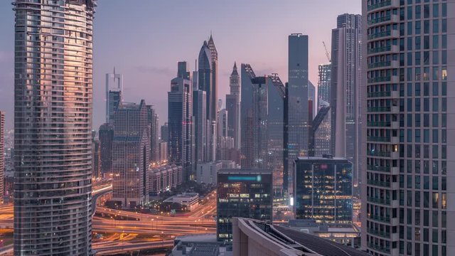 Aerial view to financial district with new towers and tall buildings with busy roads night to day transition timelapse in Dubai Downtown from above with traffic on highway, Dubai, United Arab Emirates
