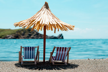 Toy chaise longue and sun umbrella on sandy beach on sunny day at the blue sea background....