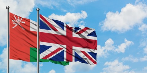 Oman and United Kingdom flag waving in the wind against white cloudy blue sky together. Diplomacy concept, international relations.