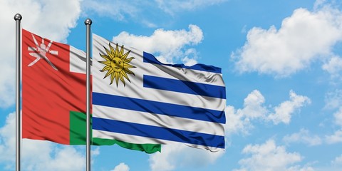 Oman and Uruguay flag waving in the wind against white cloudy blue sky together. Diplomacy concept, international relations.