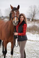 Obraz premium A beautiful girl in a fashionable shirt looks in the frame with horse in early winter. Red and black plaid shirt.