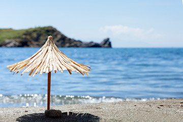 Toy sun umbrella on sandy beach on sunny day at the blue sea background. Relaxation concept.