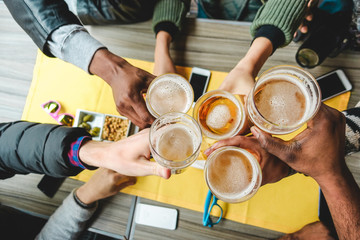 Group of friends enjoying a beer glasses in english pub restaurant - Young people cheering at vintage bar - Friendship, happy hour and party concept - Main focus on right half pint glass - obrazy, fototapety, plakaty
