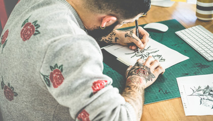Young tattoo artist drawing sketch inside ink studio - Hipster tattoer at work - Contemporary skin...