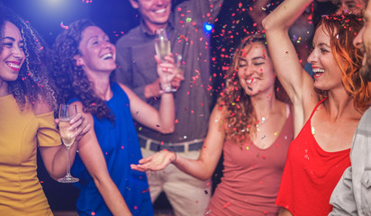 Happy friends making party throwing confetti, dancing and drinking champagne inside nightclub -...