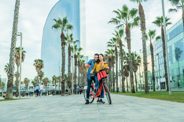 Young people making short video while riding electric bycicle in Barcelona - Happy couple having fun with new trends technology - Travel, tech and eco concept - Focus on faces - obrazy, fototapety, plakaty