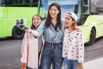 Happy asian girls making video at city bus station - Content creators friends vlogging for social network outdoor - Technology, lifestyle trends and friendship concept - Focus on faces