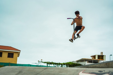 Young boy performing with kick scooter in skate park outdoor - Millennial generation person having fun with new trends - Extreme sport and youth concept - Focus on him