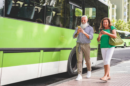 Happy senior couple using smartphones at bus station - 60's age people having fun with technology trends - Transport and joyful elderly concept - Focus on faces - Powered by Adobe