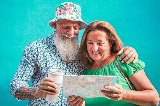 Happy senior couple reading city map with blue background - Old tourist people having fun traveling around the world - Travel, relationship and joyful elderly lifestyle concept - Focus on faces - Powered by Adobe