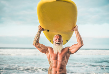 Senior trendy man doing surf with longboard - Happy old guy having fun doing extreme sport - Joyful elderly concept - Focus on his face - obrazy, fototapety, plakaty