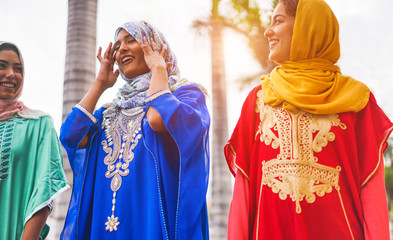 Happy muslim women walking in city center - Young arabian girls having fun together on sunny day - Friendship, youth, ethnic culture and religion dress concept - Focus on center girl face