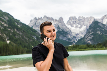 Outdoor portrait handsome man talking by phone on mountains and lake background