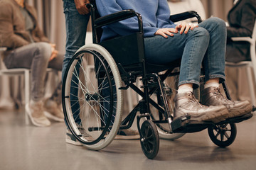 Obraz premium Close-up of young disabled woman sitting in wheelchair with other people in the background she visiting therapy lesson