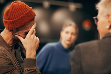 Young sad man in hat worried about his problems and visiting the lessons when people support each...