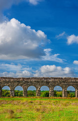 Fototapeta na wymiar Ancient roman aqueduct ruins in Rome countryside with beautiful clouds above