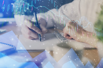 Financial forex graph displayed on hands taking notes background. Concept of research. Multi exposure