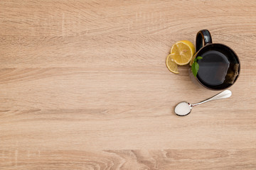 A mug of tea and lemons on the side with a spoon full of sugar on a wooden table