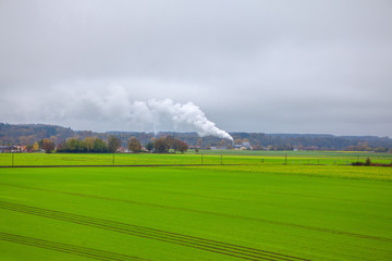 Fototapeta na wymiar ecological image with green field and white smoke from the chemical plant 