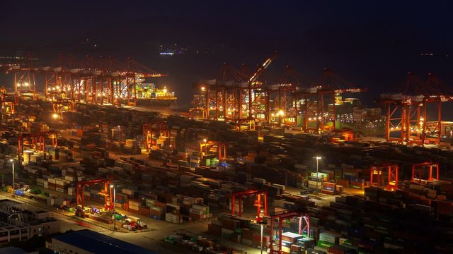 Timelapse illuminated Shanghai cranes load large cargo vessels in Yangshan Port of Shengsi against Chinese hills silhouettes at night