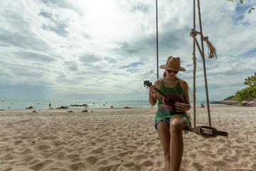 asian girls play ukulele on the beach with the sea and mountains surrounded on weekend