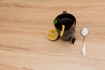 A mug of tea and lemons on the side with a spoon full of sugar on a wooden table