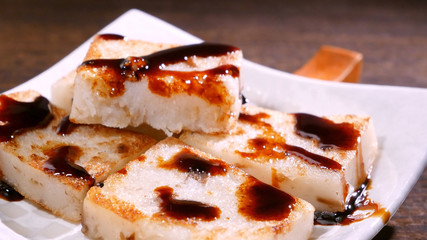 Pouring black soy sauce on ready-to-eat delicious turnip cake, Chinese traditional local dish radish cake in restaurant, close up, copy space.
