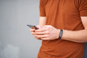 Young man using smartphone near a sloppy painted grey urban wall.