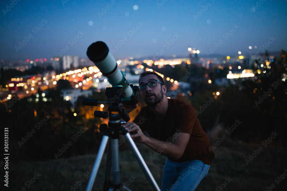 Canvas Prints astronomer with a telescope watching at the stars and moon with blurred city lights in the backgroun