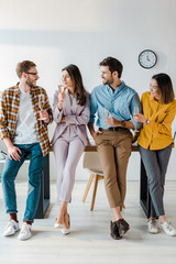 Fototapeta premium cheerful businessmen and multicultural businesswomen holding champagne glasses in office