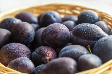 a lot of black plum with drops of water in a straw basket close-up