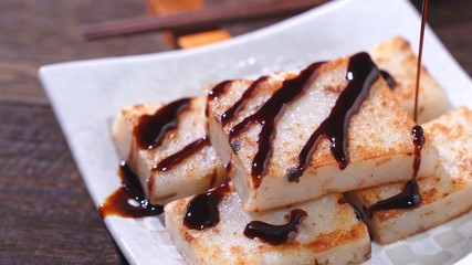 Pouring black soy sauce on ready-to-eat delicious turnip cake, Chinese traditional local dish radish cake in restaurant, close up, copy space.