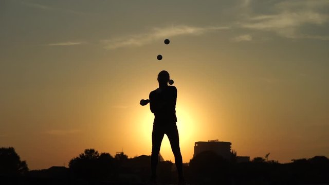 Circus artist juggling with balls on colorful sunset