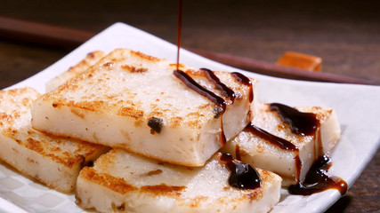 Pouring black soy sauce on ready-to-eat delicious turnip cake, Chinese traditional local dish radish cake in restaurant, close up, copy space.